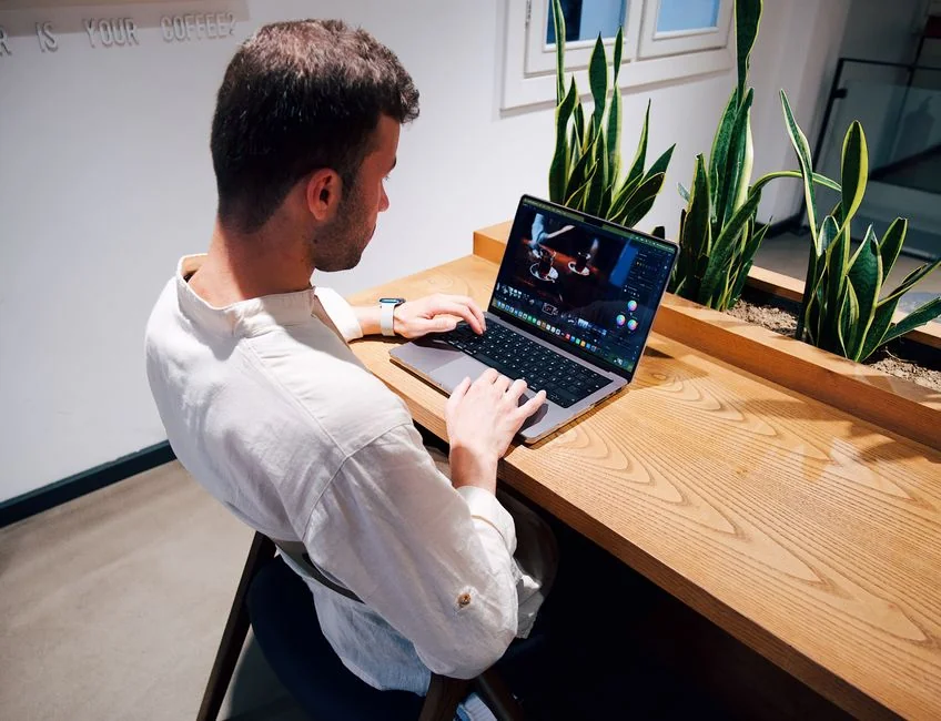 Gros plan sur des mains tapant sur un ordinateur portable, à côté d’une tasse de café posée sur un bureau en bois.